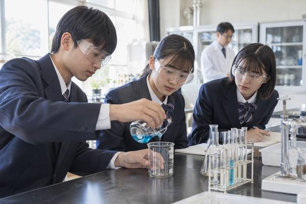 選択授業の理科実験で、安全ゴーグルを着けてビーカーを扱う制服姿の高校生3人