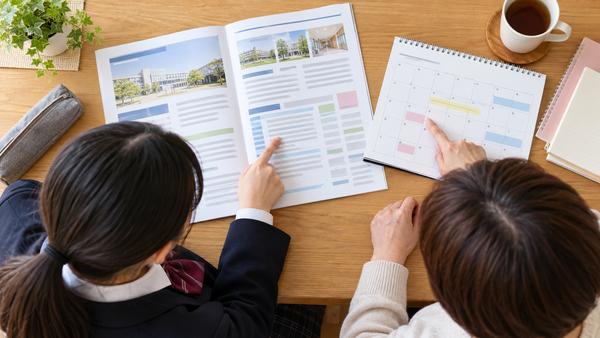 大学の募集要項とカレンダーを広げ、保護者と一緒に出願条件と日程を確認している制服の高校生