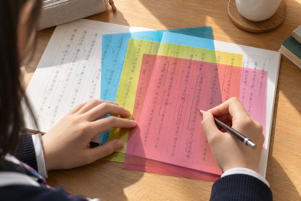 3色の透明シートを重ね、内側の層から順に印を付ける高校生の手
