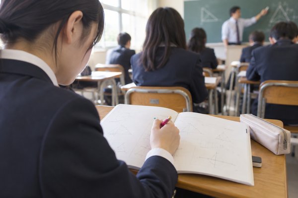 授業中にノートの止まった行へ印を付けている高校生の肩越しの手元