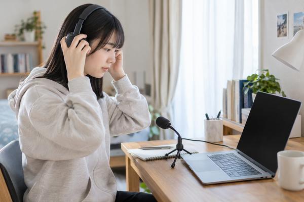 静かな部屋でヘッドホンとマイクを準備してオンラインの英語テストに備える高校生
