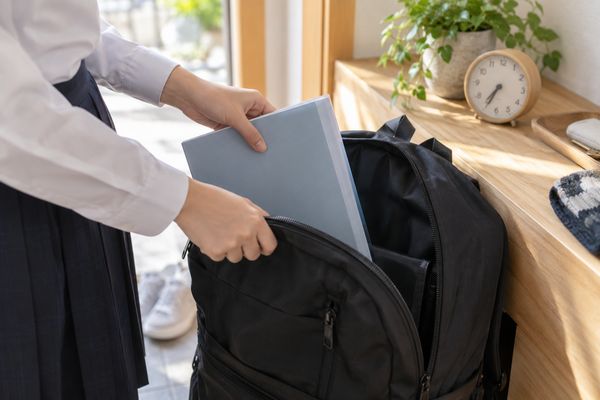 登校前の玄関で提出用ファイルを通学リュックへ入れる制服の生徒の手元