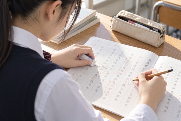 自習室で漢文の答案の誤りを消しゴムで直し、赤いペンで読む順番を書き込む高校生