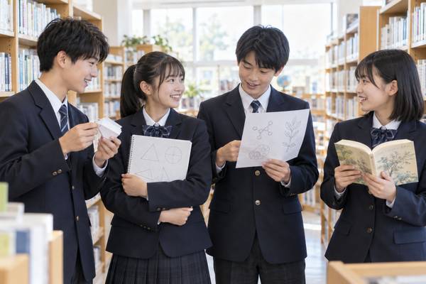 図書室で単語カードや方眼ノート、理科の図、国語の本をそれぞれ手にした中学生4人