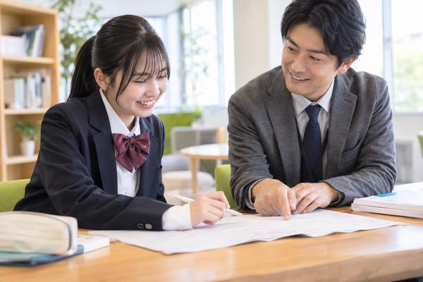 返却された答案を先生と一緒に見ながら、得点の中身を確かめる制服姿の高校生