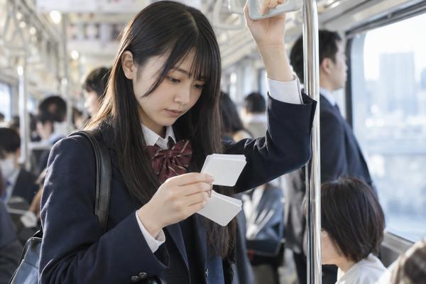 朝の通学電車でつり革につかまり単語カードをめくる制服姿の高校3年生