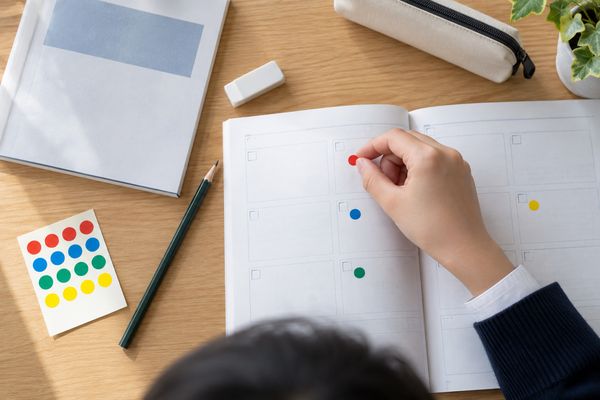 学習机で、生徒が練習プリントの問題ごとに色違いの丸シールを貼り分けている手元