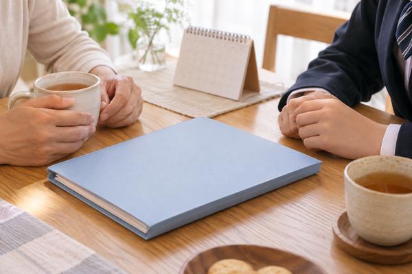 保護者と高校生が温かい飲み物を挟み、ノートを前に落ち着いて話している