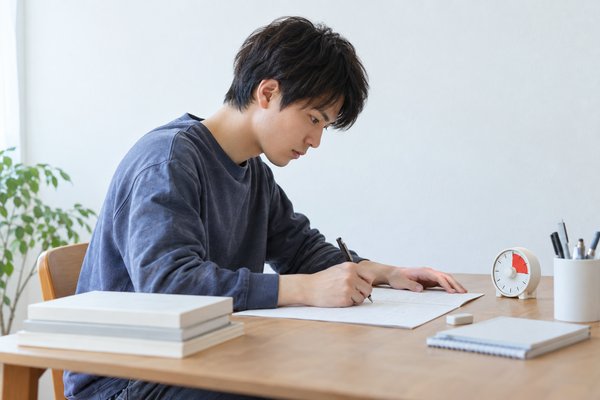 明るい自習室で、浪人生の男子がタイマーを横に置き、一問だけを時間を測って解き直している様子