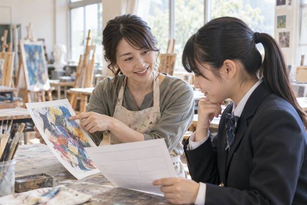 美術室で、美術の先生が制服姿の中学生に作品を示しながら、観点ごとの評価について説明している様子