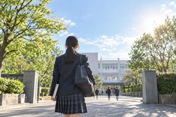 付箋をはさんだノートを持ち、朝の日差しの中を校舎へ向かって歩いていく制服姿の中学生の後ろ姿