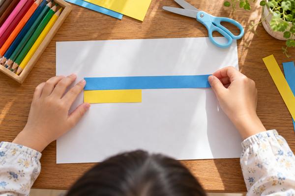 白い紙の上に、もとにする量を表す長い青のテープと、比べる量を表す短い黄色のテープを並べている子どもの手元