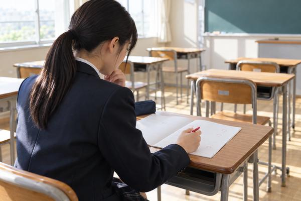 模試のあとの教室で、迷った問題に赤ペンで印を付けて復習を始める高校生