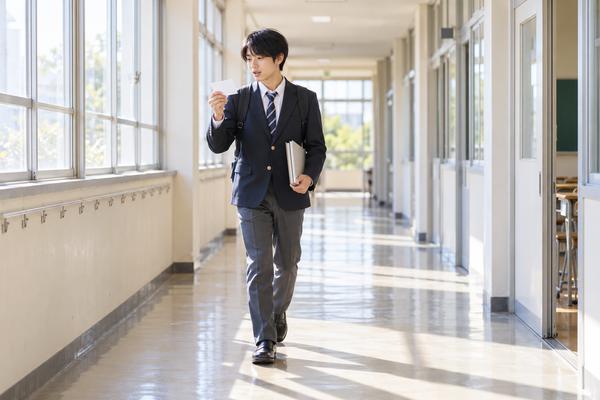 朝の校舎の廊下で、カードを見ながら疑問形と判断した根拠を声に出して確認している男子高校生