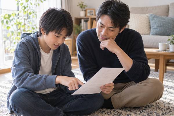 返却された答案を床に広げ、点数を責めずに中身を一緒に見ている保護者と中学生